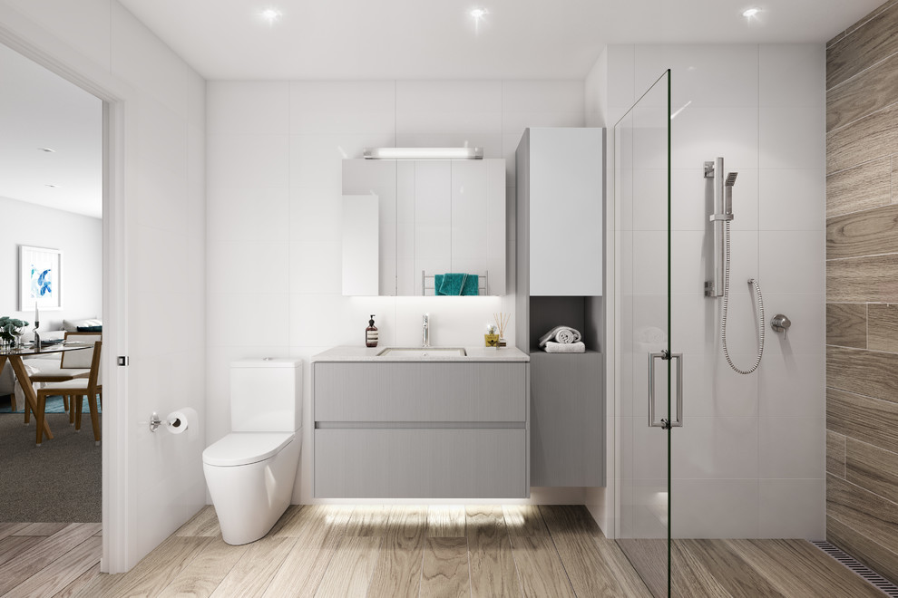 Photo of a mid-sized contemporary bathroom in Auckland with an alcove shower, a one-piece toilet, white tile, white walls, ceramic floors, an undermount sink, engineered quartz benchtops, grey cabinets, ceramic tile and a hinged shower door.