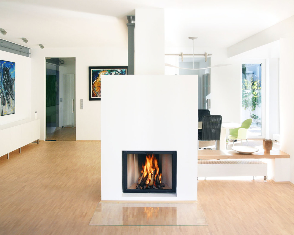 This is an example of a modern loft-style living room in Cologne with white walls, medium hardwood floors, a wood stove and a plaster fireplace surround.