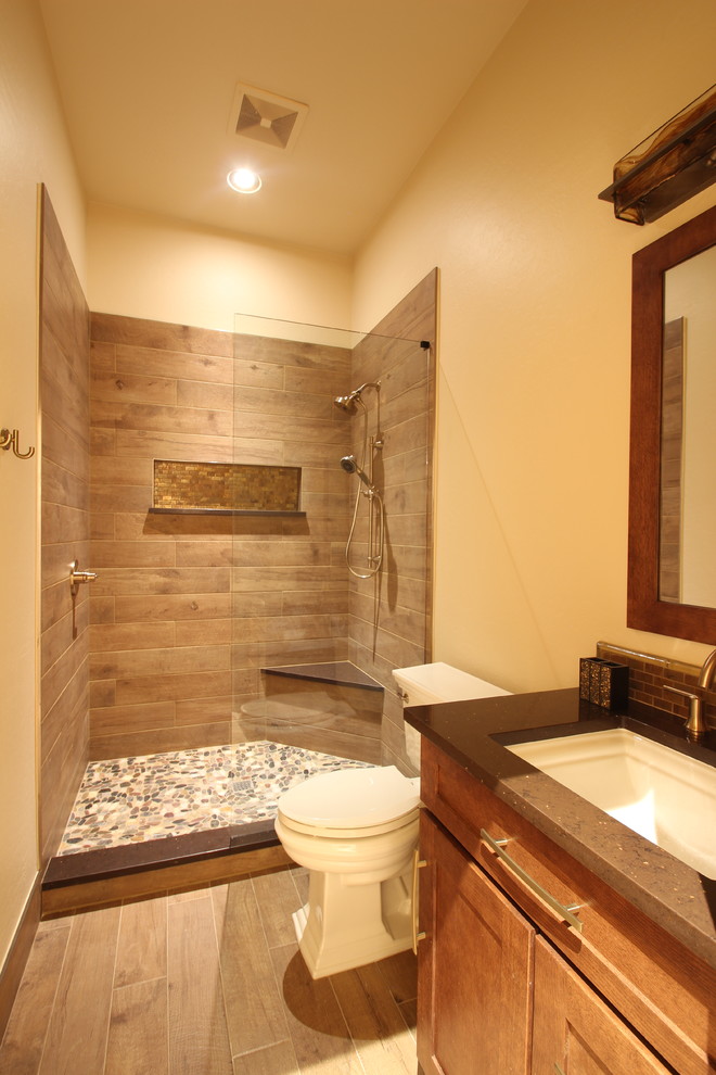 Photo of a mid-sized country 3/4 bathroom in Phoenix with shaker cabinets, medium wood cabinets, an alcove shower, a two-piece toilet, brown tile, ceramic tile, beige walls, light hardwood floors, an undermount sink, solid surface benchtops, brown floor, an open shower and brown benchtops.