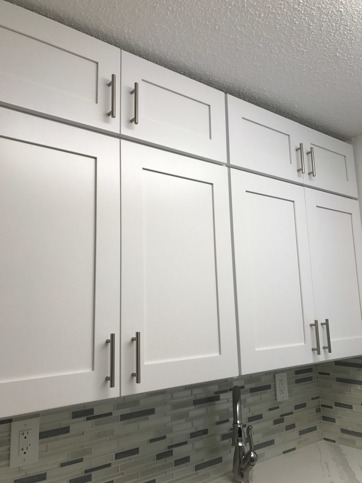 This is an example of a small modern galley separate kitchen in New York with an undermount sink, shaker cabinets, white cabinets, quartz benchtops, multi-coloured splashback, glass tile splashback, stainless steel appliances, medium hardwood floors, no island, brown floor and white benchtop.
