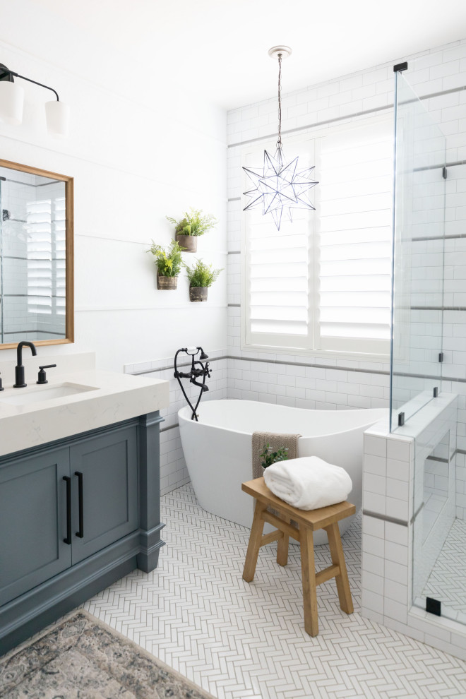 На фото: главная ванная комната в стиле неоклассика (современная классика) с фасадами в стиле шейкер, синими фасадами, отдельно стоящей ванной, столешницей из искусственного кварца, белым полом, тумбой под две раковины и напольной тумбой с