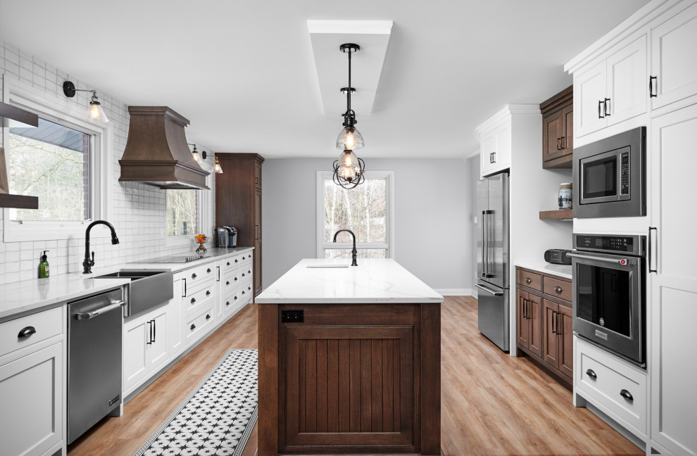 Inspiration for a transitional galley light wood floor and brown floor enclosed kitchen remodel in Toronto with a farmhouse sink, shaker cabinets, white cabinets, quartzite countertops, white backsplash, subway tile backsplash, stainless steel appliances, an island and white countertops