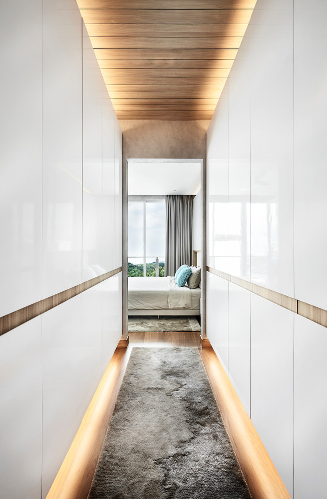 Photo of a contemporary gender-neutral walk-in wardrobe in Singapore with flat-panel cabinets, white cabinets, medium hardwood floors and brown floor.