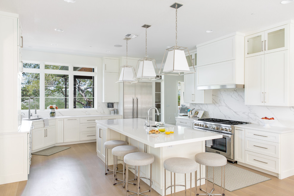 Photo of a transitional l-shaped kitchen in Austin with an undermount sink, white cabinets, white splashback, light hardwood floors, with island, beige floor and shaker cabinets.
