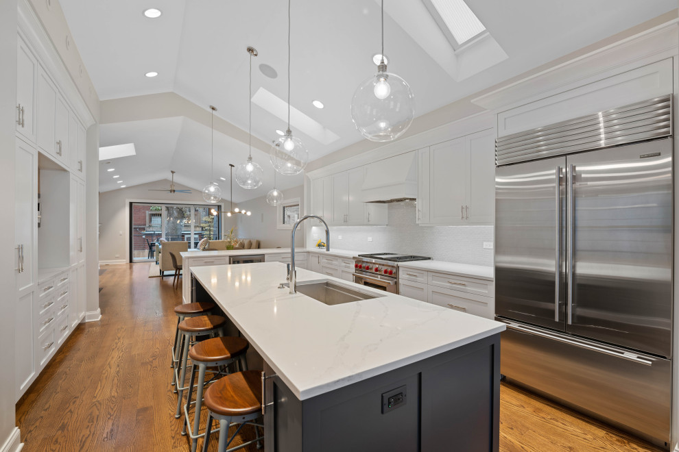 Inspiration for a large traditional l-shaped kitchen/diner in Chicago with a submerged sink, recessed-panel cabinets, white cabinets, engineered stone countertops, white splashback, stone tiled splashback, stainless steel appliances, laminate floors, an island, brown floors, white worktops and a vaulted ceiling.