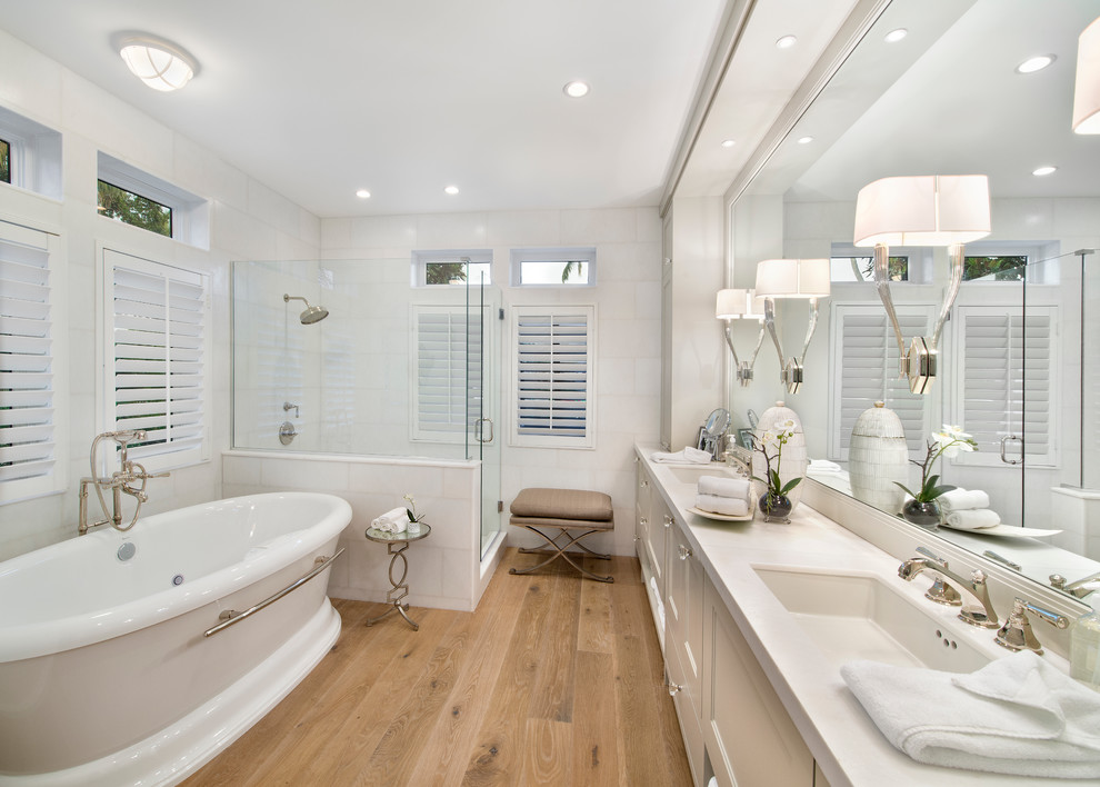 Tropical bathroom in Other with an undermount sink, recessed-panel cabinets, white cabinets, a freestanding tub, a corner shower, white tile, white walls and medium hardwood floors.