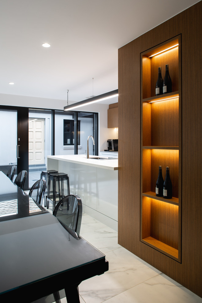 Inspiration for a mid-sized contemporary kitchen in Adelaide with brown cabinets, solid surface benchtops, grey splashback, ceramic splashback, black appliances, marble floors, with island, grey floor and white benchtop.