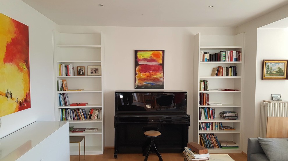 Mid-sized modern open concept family room in Munich with a library, white walls, light hardwood floors, a plaster fireplace surround and no tv.