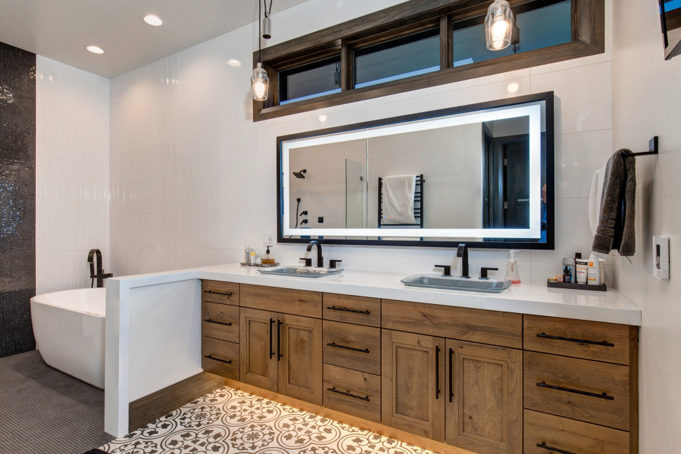 Inspiration for a country bathroom in Salt Lake City with recessed-panel cabinets, medium wood cabinets, a freestanding tub, white tile, a drop-in sink, multi-coloured floor, white benchtops, a double vanity and a floating vanity.
