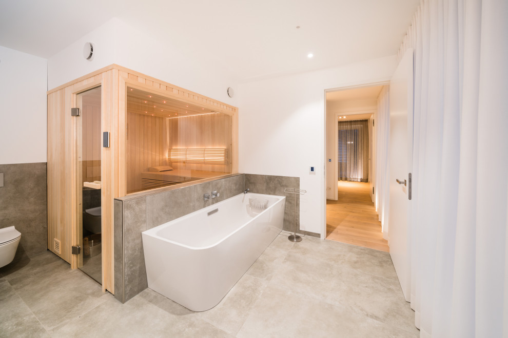 Photo of a mid-sized contemporary bathroom in Frankfurt with a corner tub, a wall-mount toilet, white walls, with a sauna, a wall-mount sink and grey floor.