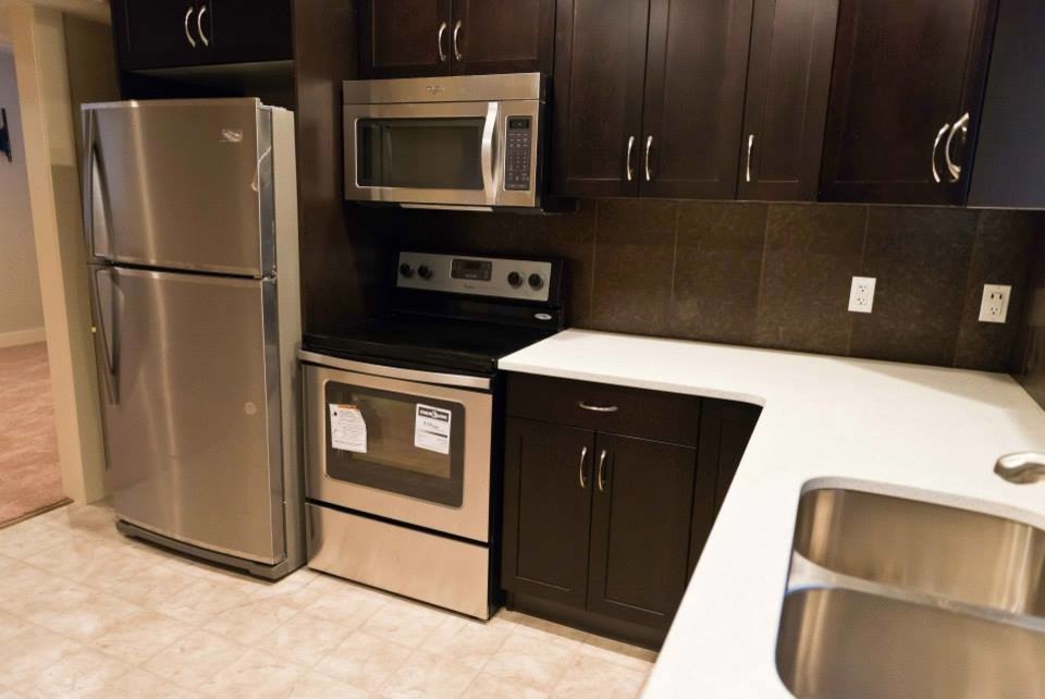 Inspiration for a small transitional l-shaped ceramic tile enclosed kitchen remodel in Edmonton with a double-bowl sink, recessed-panel cabinets, dark wood cabinets, solid surface countertops, brown backsplash, ceramic backsplash, stainless steel appliances and no island