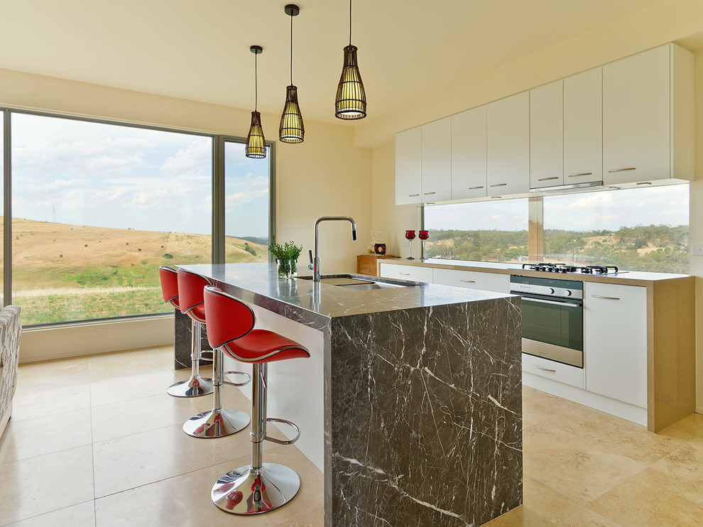 Contemporary open plan kitchen in Melbourne with a double-bowl sink, raised-panel cabinets, white cabinets, marble benchtops, travertine floors, with island and stainless steel appliances.