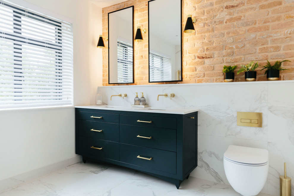 Photo of a large transitional master bathroom in London with flat-panel cabinets, blue cabinets, an open shower, a wall-mount toilet, white tile, marble, white walls, marble floors, a drop-in sink, marble benchtops, white floor, an open shower, white benchtops, a double vanity, a built-in vanity and brick walls.