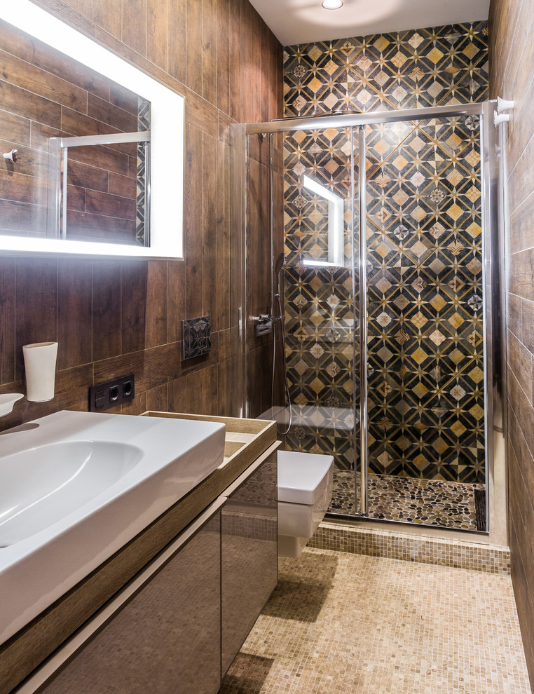 Design ideas for a contemporary 3/4 bathroom in Other with flat-panel cabinets, an alcove shower, brown tile, black tile, mosaic tile floors, beige floor, a sliding shower screen, brown cabinets, a wall-mount toilet, brown walls and a vessel sink.