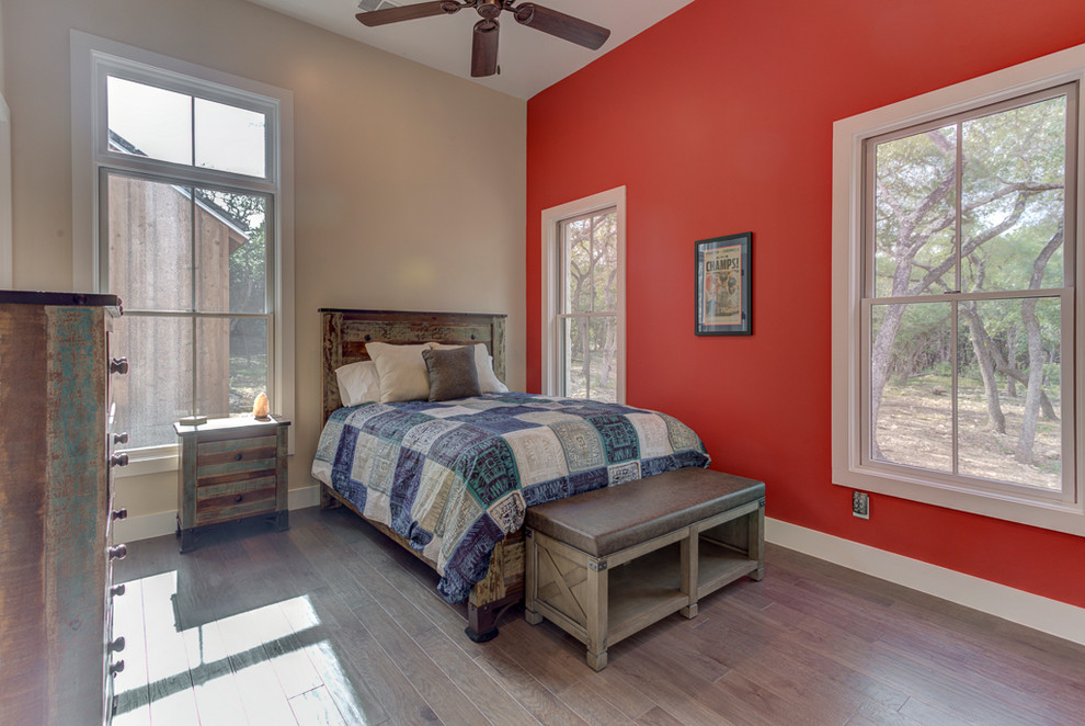 Photo of a mid-sized country guest bedroom in Austin with red walls, medium hardwood floors, no fireplace and brown floor.