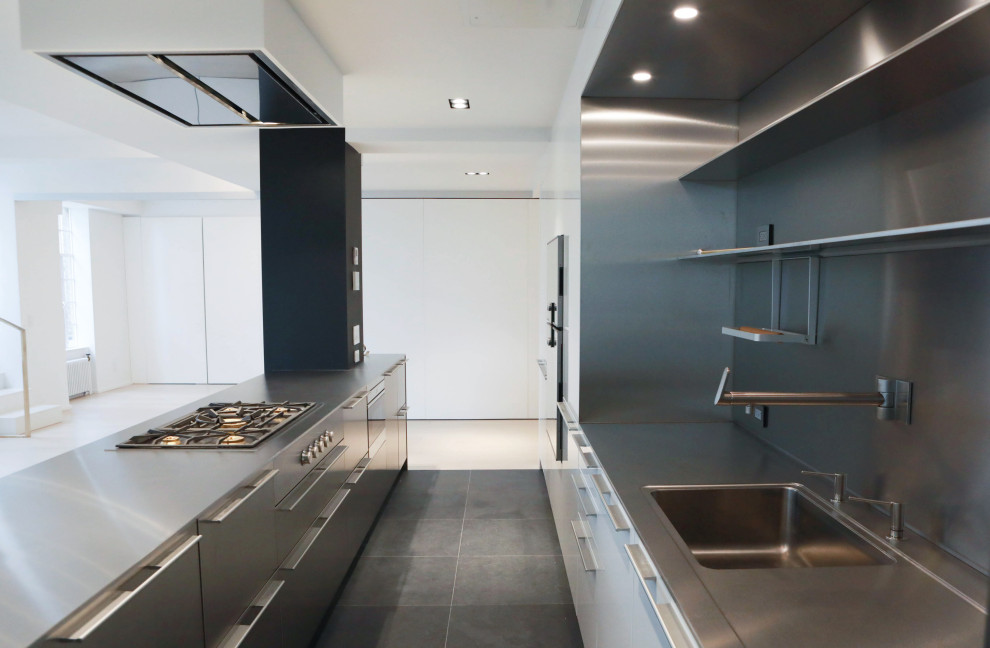 This is an example of a large industrial galley eat-in kitchen in New York with an undermount sink, stainless steel cabinets, stainless steel benchtops, metallic splashback, stainless steel appliances, porcelain floors, multiple islands and grey floor.