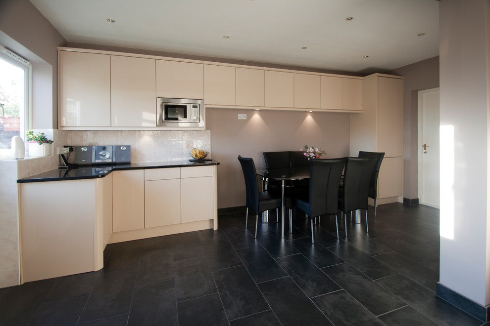 Design ideas for a large contemporary u-shaped eat-in kitchen in Surrey with a drop-in sink, flat-panel cabinets, beige cabinets, granite benchtops, beige splashback, ceramic splashback, stainless steel appliances, ceramic floors, no island, black floor and black benchtop.