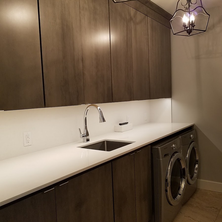 Photo of a mid-sized contemporary galley utility room with an undermount sink, flat-panel cabinets, a side-by-side washer and dryer, quartz benchtops, dark wood cabinets, beige walls, porcelain floors and beige floor.
