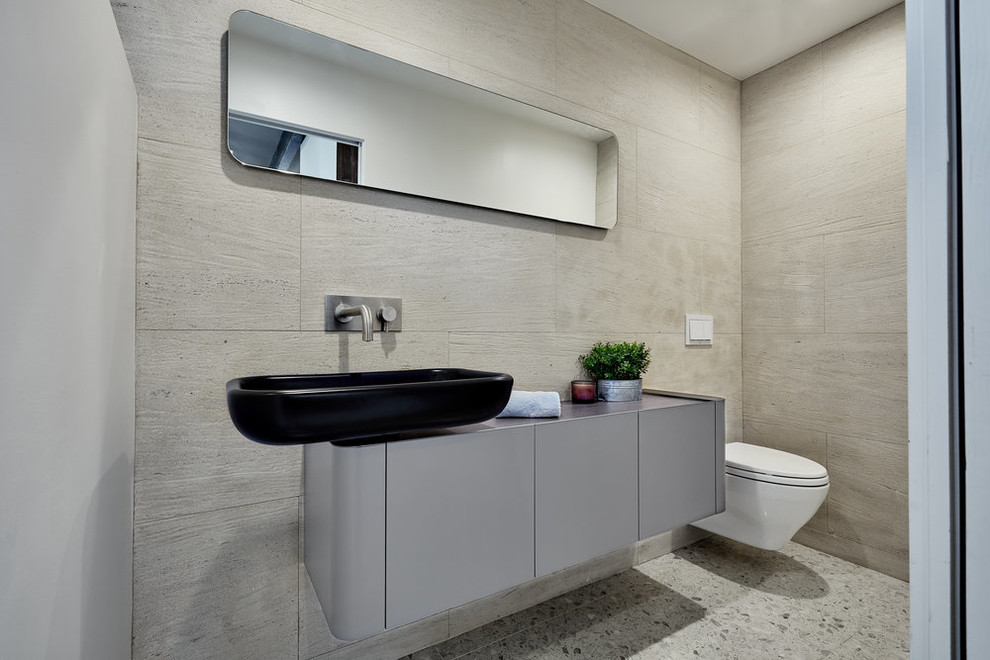 This is an example of a midcentury powder room in Los Angeles with flat-panel cabinets, grey cabinets, a wall-mount toilet, gray tile, a vessel sink and grey floor.
