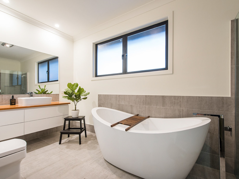 Large contemporary master bathroom in Brisbane with white cabinets, a freestanding tub, a curbless shower, white walls, a vessel sink, wood benchtops, grey floor, recessed-panel cabinets, a two-piece toilet, brown tile, ceramic tile, concrete floors, an open shower and white benchtops.