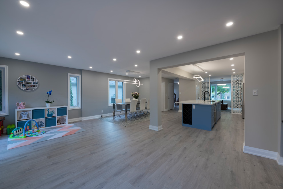 This is an example of a large contemporary single-wall eat-in kitchen in Toronto with an undermount sink, shaker cabinets, blue cabinets, grey splashback, ceramic splashback, stainless steel appliances, light hardwood floors, with island, grey floor and recessed.