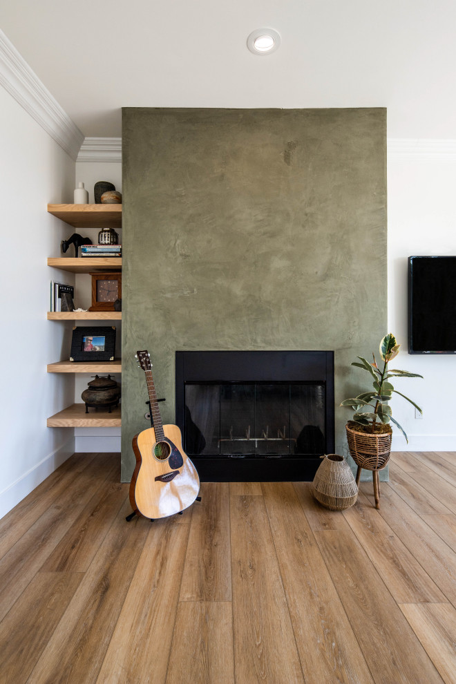 Mid-sized midcentury formal open concept living room in San Diego with green walls, laminate floors, a standard fireplace, a plaster fireplace surround, a corner tv, brown floor and wood walls.