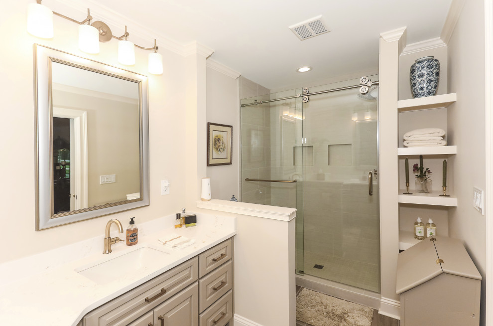 Design ideas for a medium sized classic ensuite bathroom in Atlanta with raised-panel cabinets, an alcove shower, a two-piece toilet, porcelain tiles, beige walls, porcelain flooring, a submerged sink, engineered stone worktops, beige floors, a sliding door, white worktops, double sinks, a built in vanity unit and a wall niche.