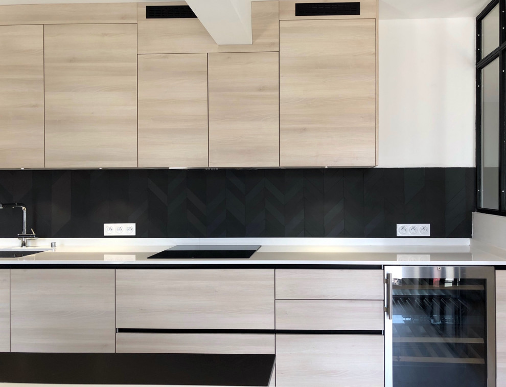 Large contemporary u-shaped separate kitchen in Paris with an undermount sink, light wood cabinets, quartzite benchtops, black splashback, ceramic splashback, black appliances, with island, white benchtop, flat-panel cabinets, light hardwood floors and brown floor.