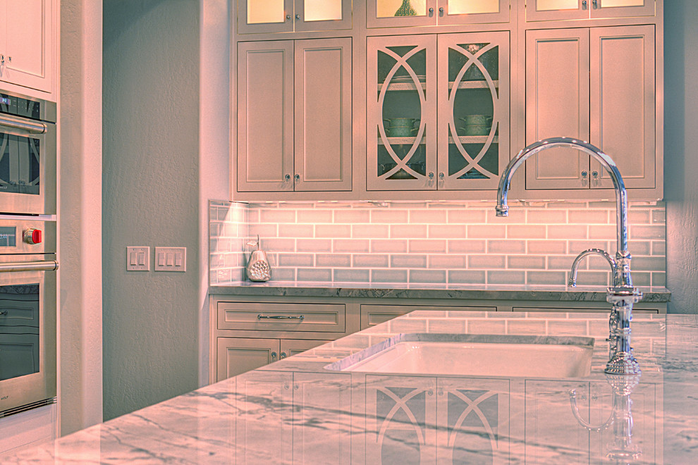 Inspiration for a large transitional l-shaped medium tone wood floor kitchen remodel in Phoenix with an undermount sink, recessed-panel cabinets, white cabinets, gray backsplash, subway tile backsplash, stainless steel appliances and an island