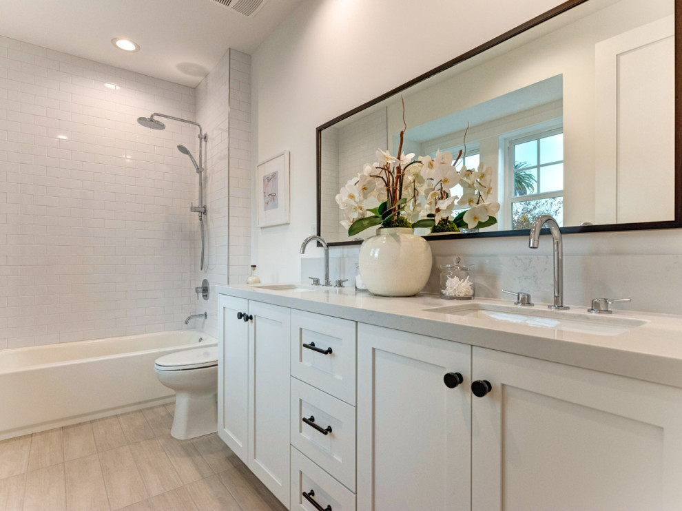 This is an example of a nautical ensuite bathroom in Los Angeles with shaker cabinets, white cabinets, a wall mounted toilet, white tiles, white walls, a submerged sink, engineered stone worktops, grey floors, grey worktops, double sinks and a built in vanity unit.