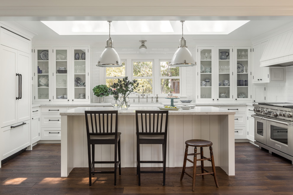This is an example of a mid-sized country u-shaped kitchen in San Francisco with glass-front cabinets, white cabinets, white splashback, stainless steel appliances, dark hardwood floors and with island.