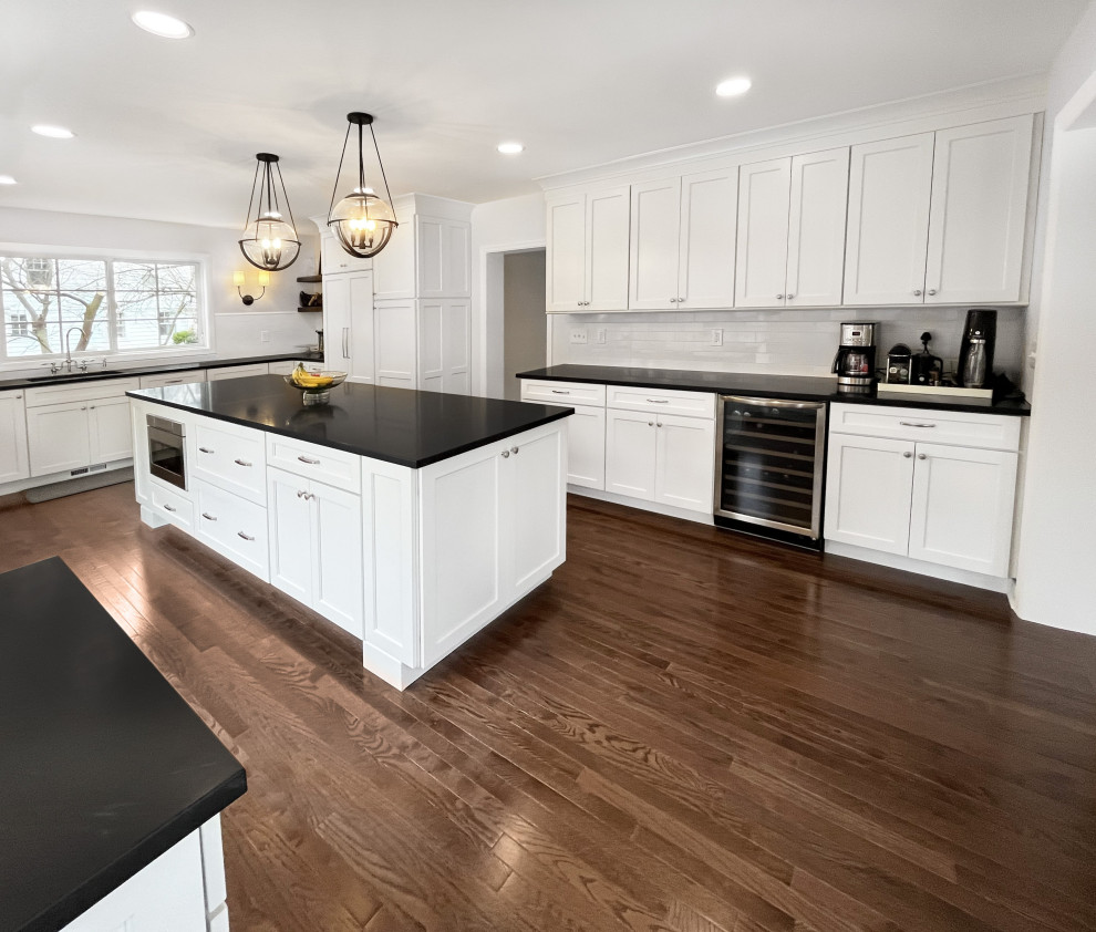 Example of a large transitional medium tone wood floor and brown floor kitchen design in Philadelphia with an undermount sink, shaker cabinets, white cabinets, soapstone countertops, white backsplash, porcelain backsplash, paneled appliances, an island and black countertops