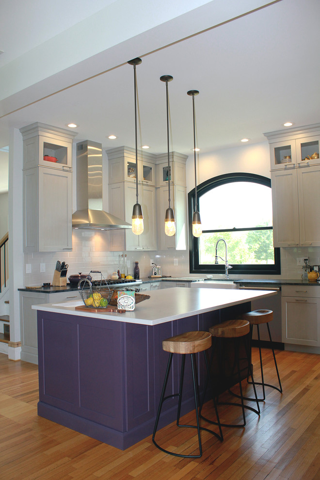 Design ideas for a large transitional l-shaped open plan kitchen in Boston with a farmhouse sink, recessed-panel cabinets, grey cabinets, soapstone benchtops, grey splashback, ceramic splashback, stainless steel appliances, medium hardwood floors, with island, brown floor and black benchtop.