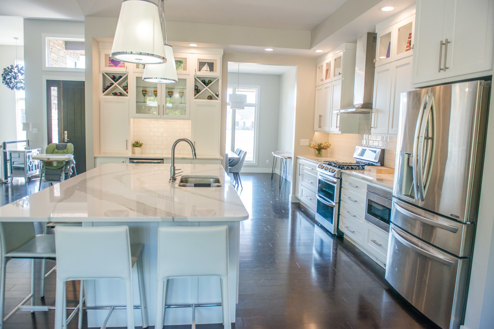 Open concept kitchen - huge transitional l-shaped dark wood floor and brown floor open concept kitchen idea in Chicago with a double-bowl sink, shaker cabinets, white cabinets, quartz countertops, white backsplash, ceramic backsplash, stainless steel appliances and an island