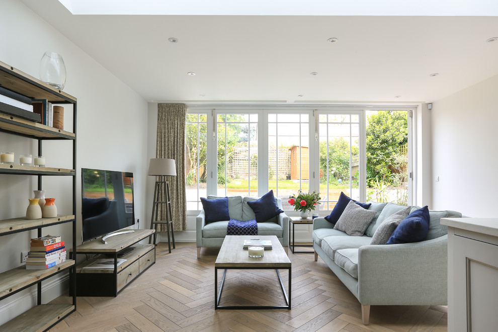 Photo of a transitional family room in London with white walls, medium hardwood floors, a freestanding tv and brown floor.