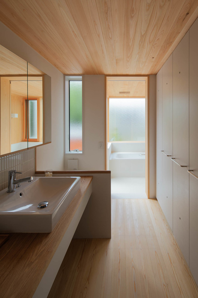 This is an example of a mid-sized scandinavian powder room in Yokohama with flat-panel cabinets, white cabinets, a one-piece toilet, white tile, matchstick tile, white walls, light hardwood floors, a pedestal sink, wood benchtops and beige floor.