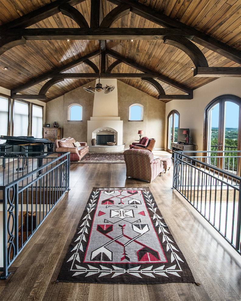 This is an example of a loft-style living room in Austin with beige walls, dark hardwood floors, a standard fireplace, a plaster fireplace surround and a freestanding tv.