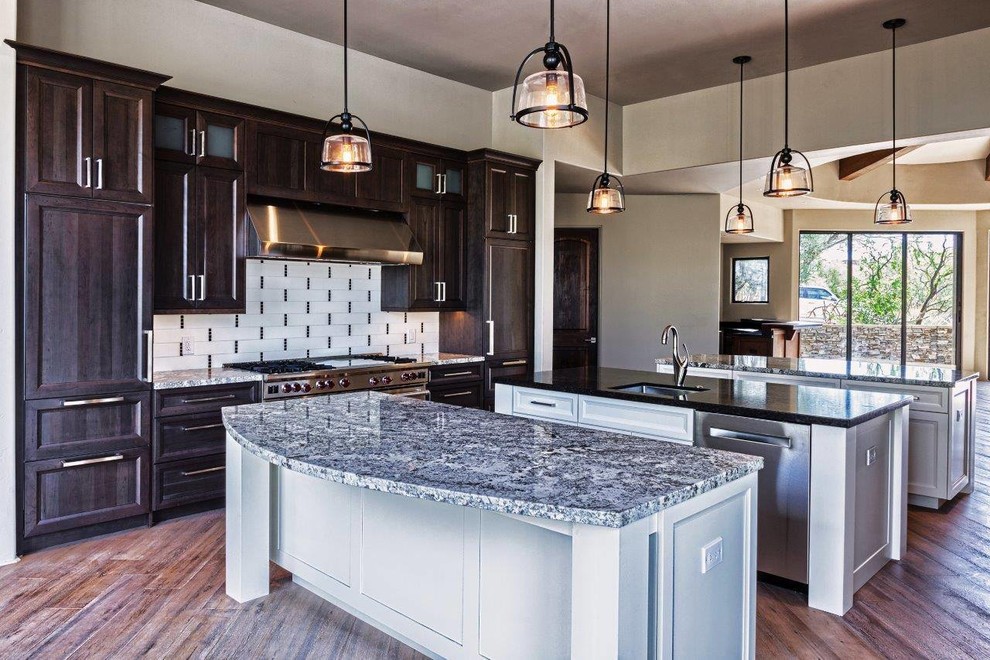 Inspiration for a large transitional medium tone wood floor kitchen remodel in Phoenix with an undermount sink, recessed-panel cabinets, dark wood cabinets, granite countertops, white backsplash, porcelain backsplash, two islands and paneled appliances