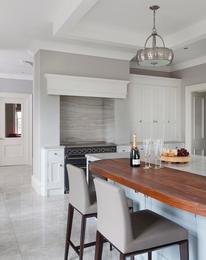 This is an example of an expansive traditional l-shaped open plan kitchen in Other with a farmhouse sink, shaker cabinets, blue cabinets, marble benchtops, grey splashback, stone slab splashback, black appliances, ceramic floors and with island.
