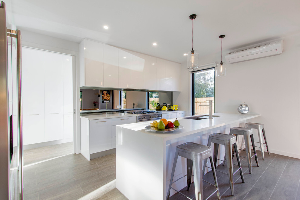 Mid-sized contemporary single-wall open plan kitchen in Melbourne with an undermount sink, flat-panel cabinets, white cabinets, mirror splashback, stainless steel appliances and a peninsula.