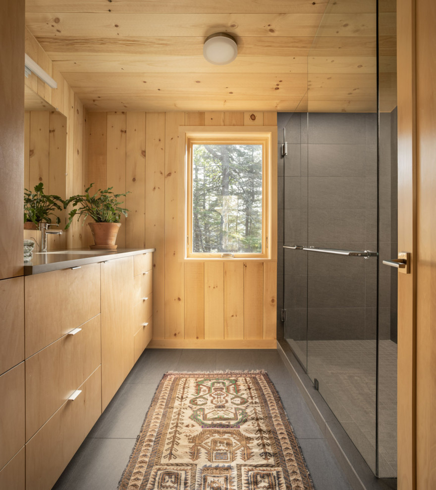 Photo of a mid-sized country master bathroom in Portland Maine with flat-panel cabinets, medium wood cabinets, an alcove shower, a one-piece toilet, gray tile, porcelain tile, brown walls, porcelain floors, an undermount sink, engineered quartz benchtops, grey floor, a hinged shower door and grey benchtops.