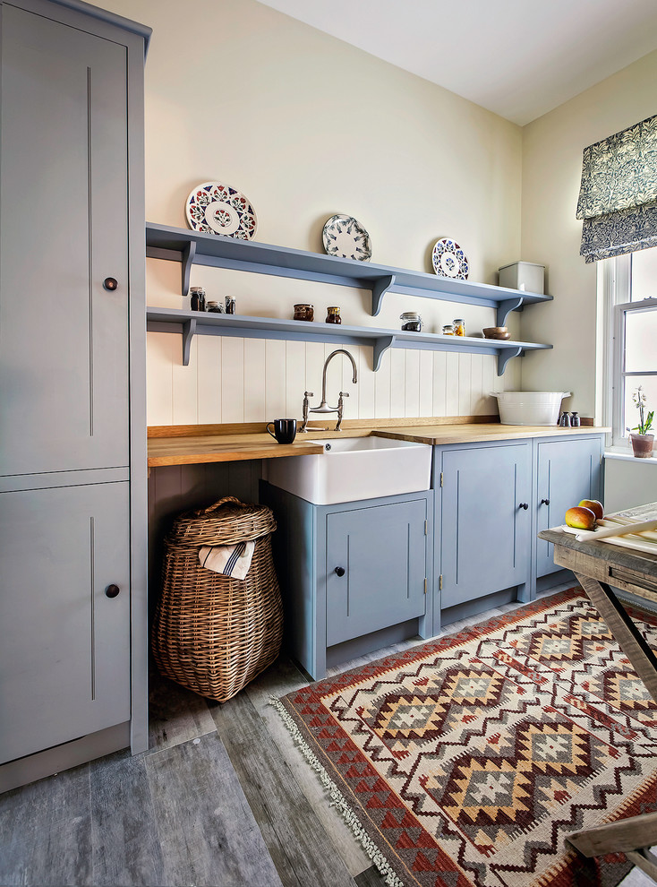 This is an example of a country kitchen in London with a farmhouse sink, shaker cabinets, blue cabinets, wood benchtops, panelled appliances and dark hardwood floors.