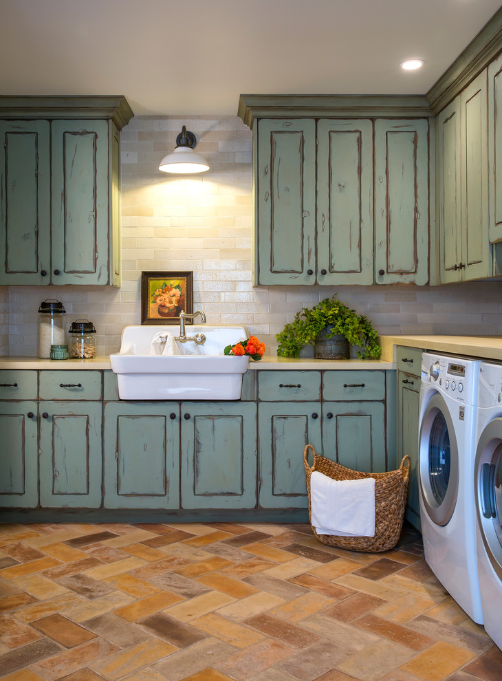 This is an example of a large mediterranean dedicated laundry room in Phoenix with a farmhouse sink, raised-panel cabinets, green cabinets, concrete benchtops, white walls, terra-cotta floors, a side-by-side washer and dryer and multi-coloured floor.