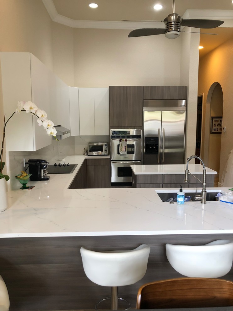 This is an example of a large modern u-shaped eat-in kitchen in Miami with a single-bowl sink, flat-panel cabinets, medium wood cabinets, quartz benchtops, white splashback, stone slab splashback, stainless steel appliances, marble floors, a peninsula, beige floor and white benchtop.