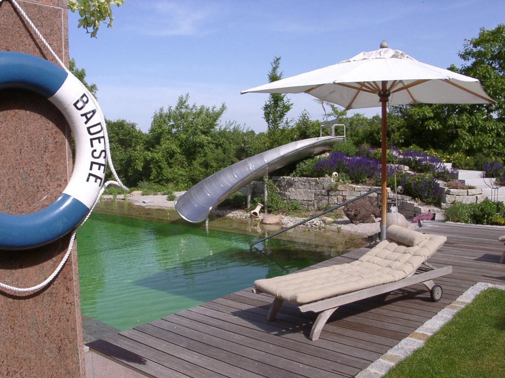 Großer Mediterraner Schwimmteich neben dem Haus in individueller Form mit Wasserrutsche und Natursteinplatten in Nürnberg