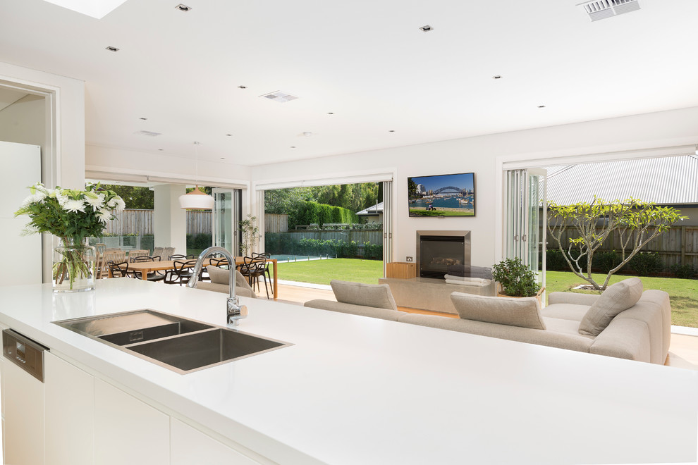 This is an example of a contemporary single-wall open plan kitchen in Sydney with a drop-in sink, flat-panel cabinets, white cabinets, granite benchtops, panelled appliances and with island.