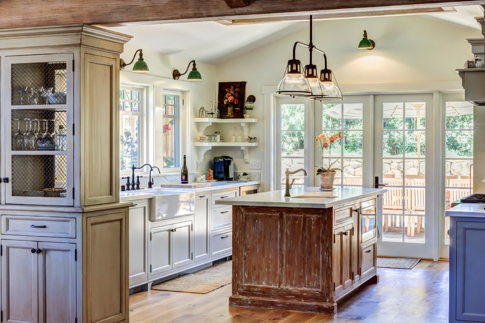Inspiration for a country u-shaped kitchen in Santa Barbara with a farmhouse sink, recessed-panel cabinets, white cabinets, medium hardwood floors, with island, brown floor and white benchtop.