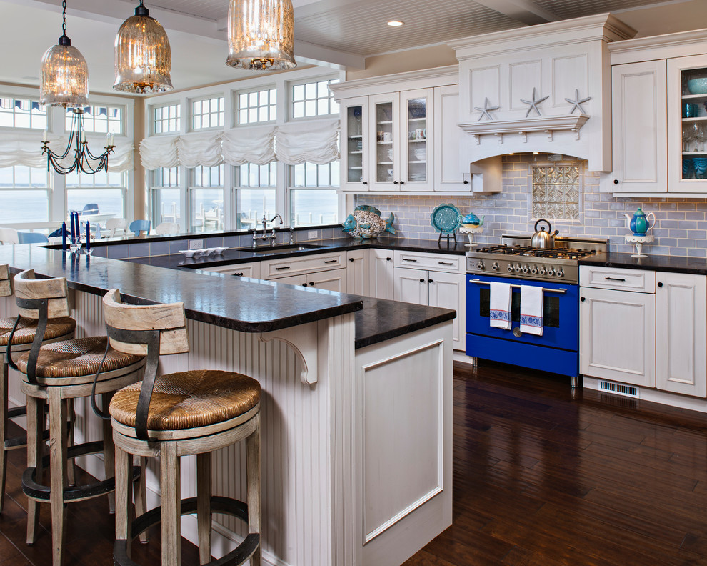 This is an example of a beach style eat-in kitchen in New York with glass-front cabinets, white cabinets, blue splashback, subway tile splashback and coloured appliances.