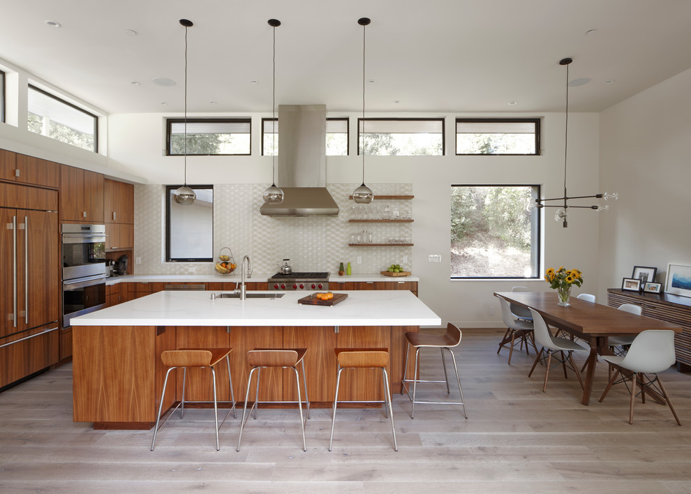 Inspiration for a large contemporary l-shaped eat-in kitchen in San Francisco with an undermount sink, flat-panel cabinets, medium wood cabinets, quartz benchtops, white splashback, glass tile splashback, stainless steel appliances, light hardwood floors and with island.