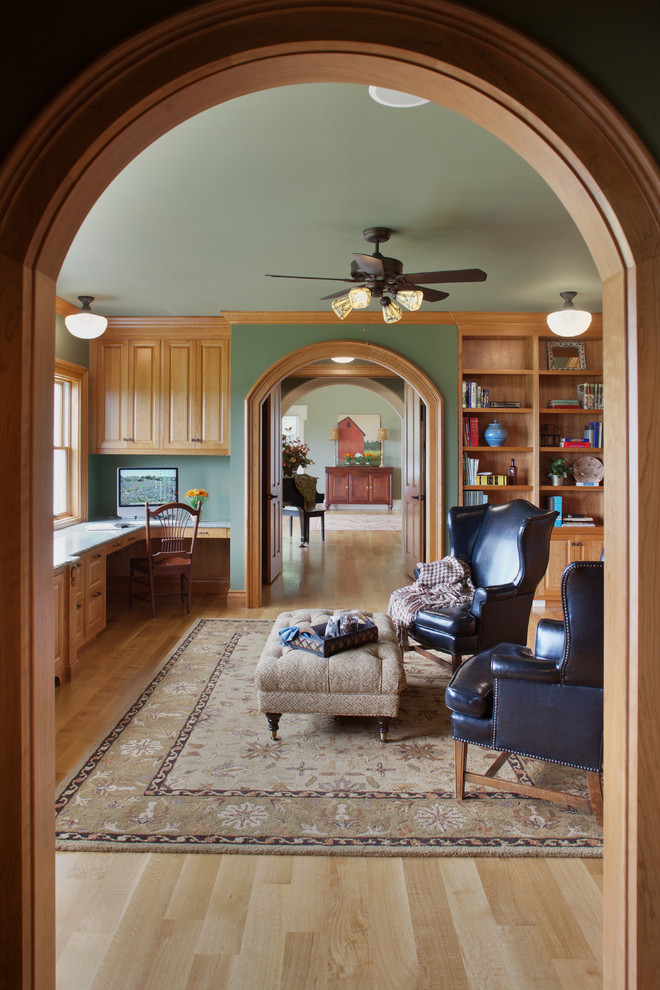 This is an example of a large traditional home office in Detroit with a library, green walls, medium hardwood floors, a built-in desk and beige floor.
